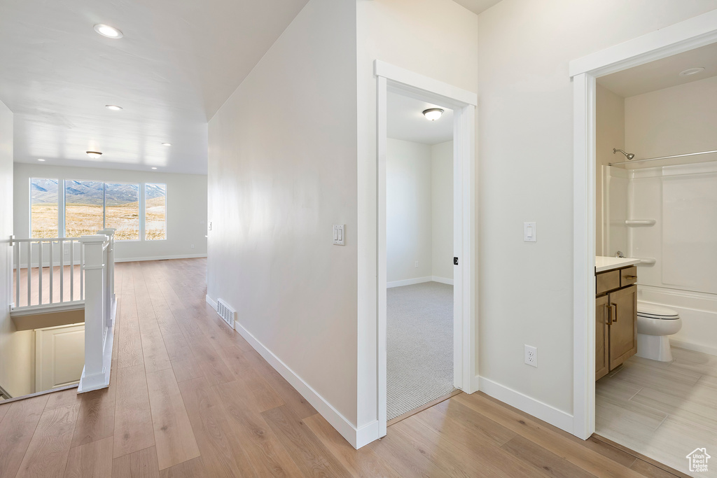Corridor with an upstairs landing, light wood finished floors, recessed lighting, and baseboards