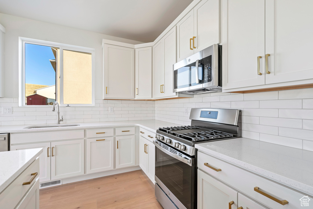 Kitchen with stainless steel appliances, a sink, white cabinets, light wood finished floors, and light stone countertops