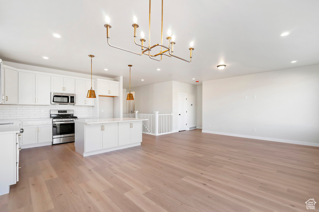 Kitchen with appliances with stainless steel finishes, decorative backsplash, open floor plan, light wood-type flooring, and recessed lighting