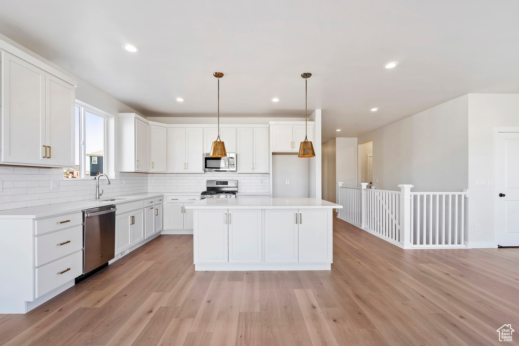 Kitchen with appliances with stainless steel finishes, backsplash, white cabinetry, light wood-style flooring, and light countertops