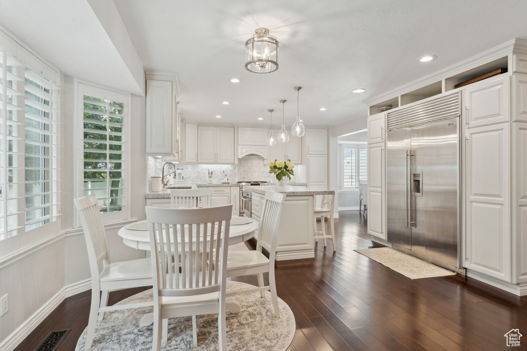 Dining room featuring healthy amount of natural light, dark wood-style flooring, baseboards, a chandelier, and recessed lighting