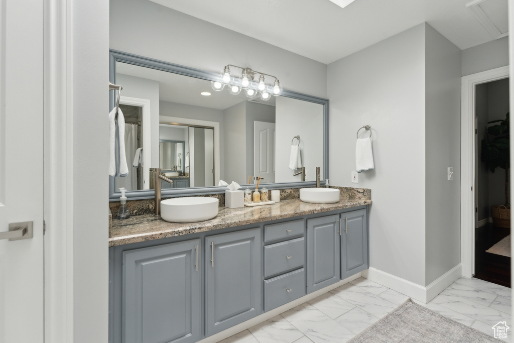 Full bathroom featuring marble look tile flooring, double vanity, and baseboards