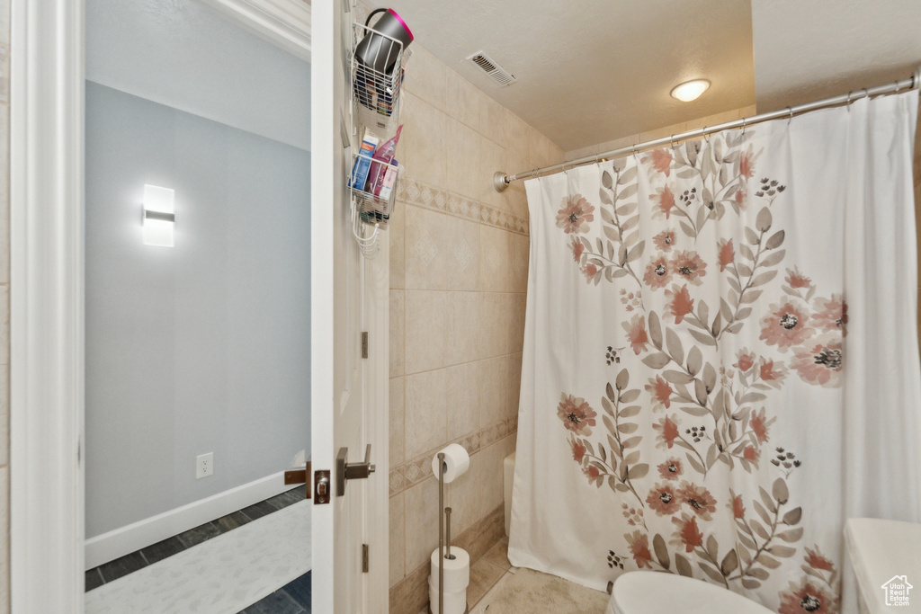 Bathroom with curtained shower, toilet, and tile patterned flooring