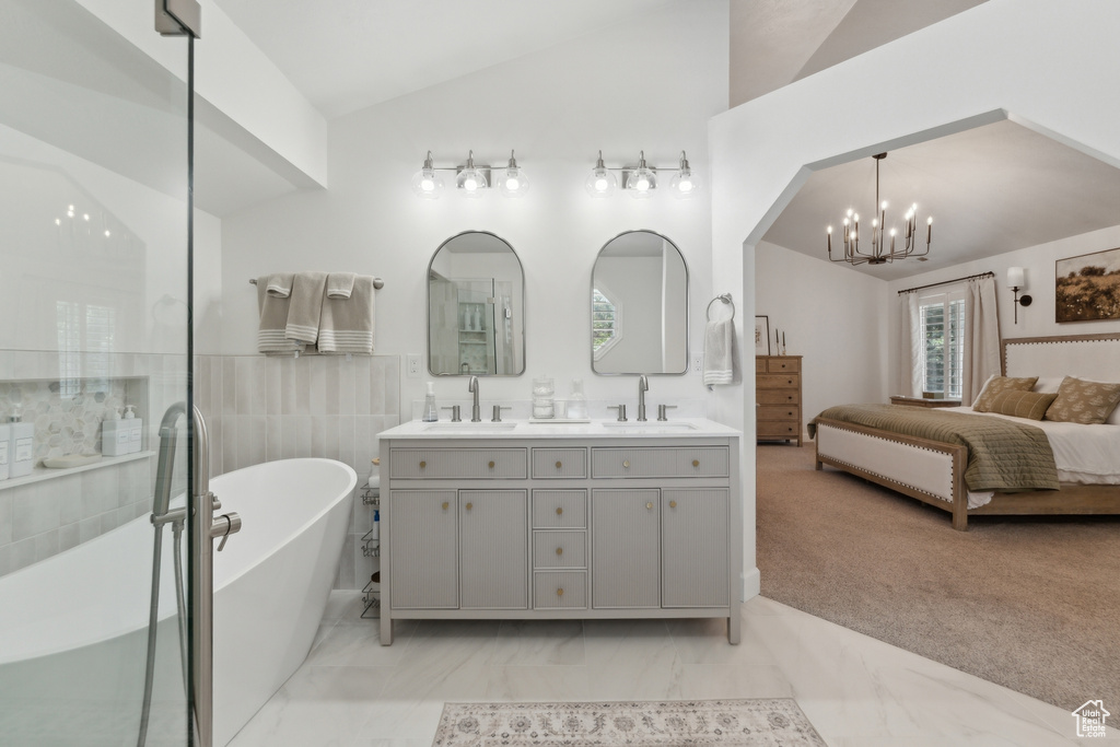 Ensuite bathroom featuring double vanity, a freestanding tub, lofted ceiling, a chandelier, and marble finish floors