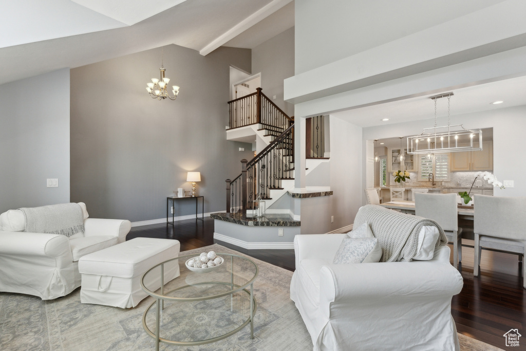 Living area with a chandelier, wood finished floors, stairs, baseboards, and high vaulted ceiling