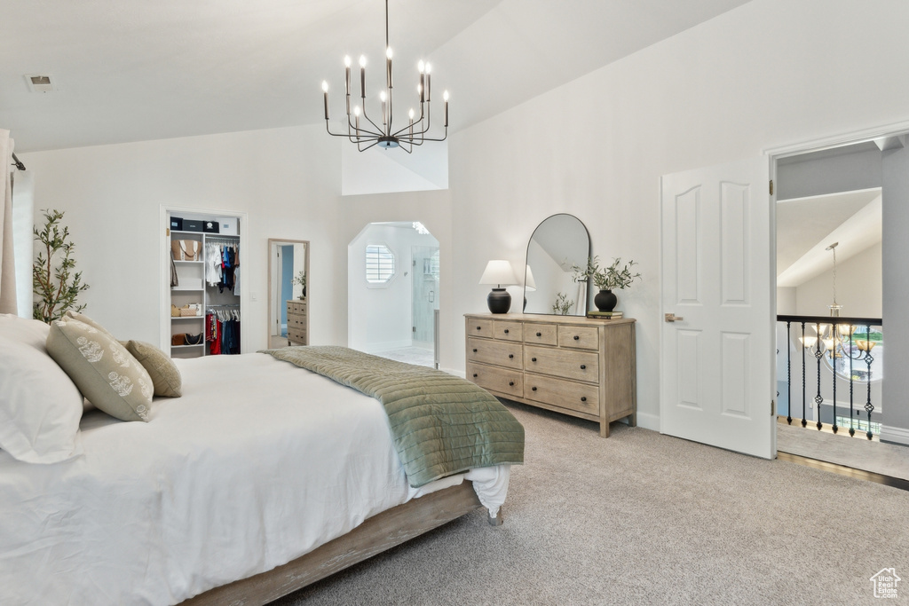 Carpeted bedroom with a chandelier, arched walkways, a walk in closet, high vaulted ceiling, and a closet