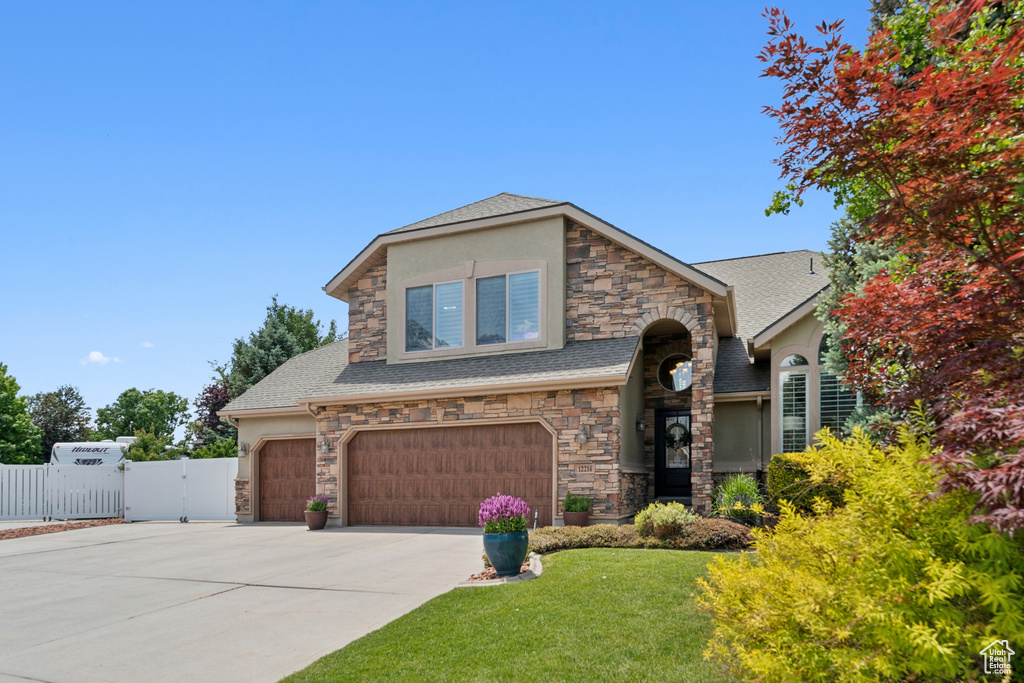 View of front of property with stone siding, a gate, driveway, and an attached garage