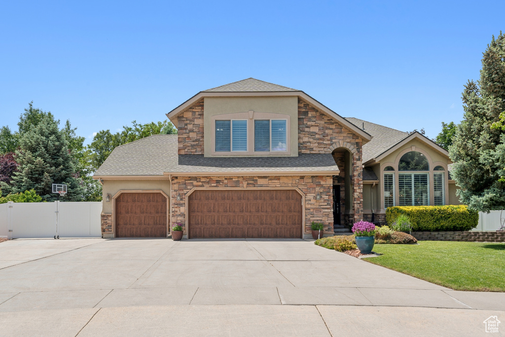 View of front of house with stone siding, stucco siding, concrete driveway, and a gate