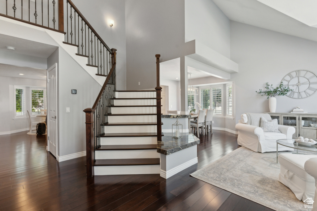 Stairs with a high ceiling, plenty of natural light, wood-type flooring, baseboards, and a chandelier