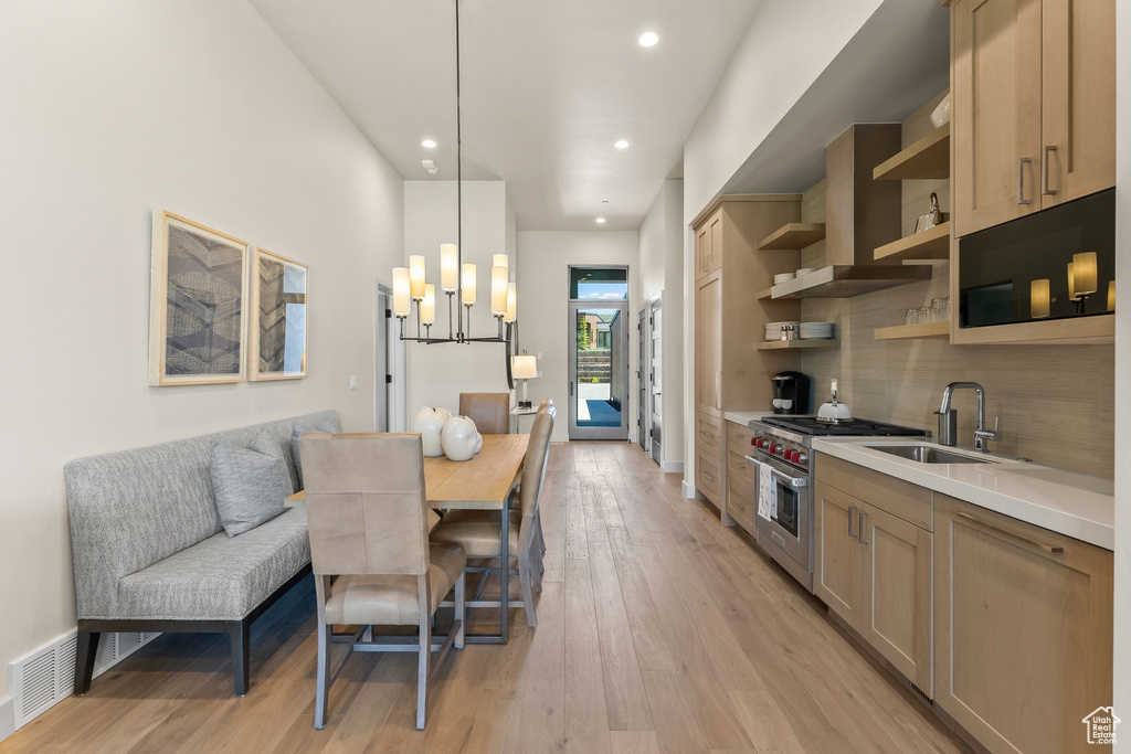 Kitchen featuring a sink, luxury range, open shelves, light wood-style floors, and tasteful backsplash
