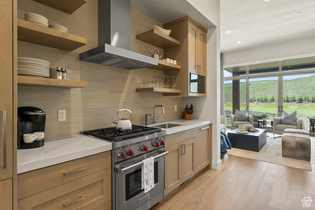 Kitchen with open shelves, wall chimney range hood, luxury stove, a sink, and decorative backsplash
