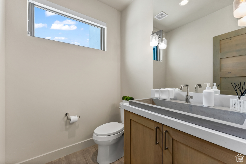 Bathroom with wood finished floors, toilet, vanity, baseboards, and recessed lighting