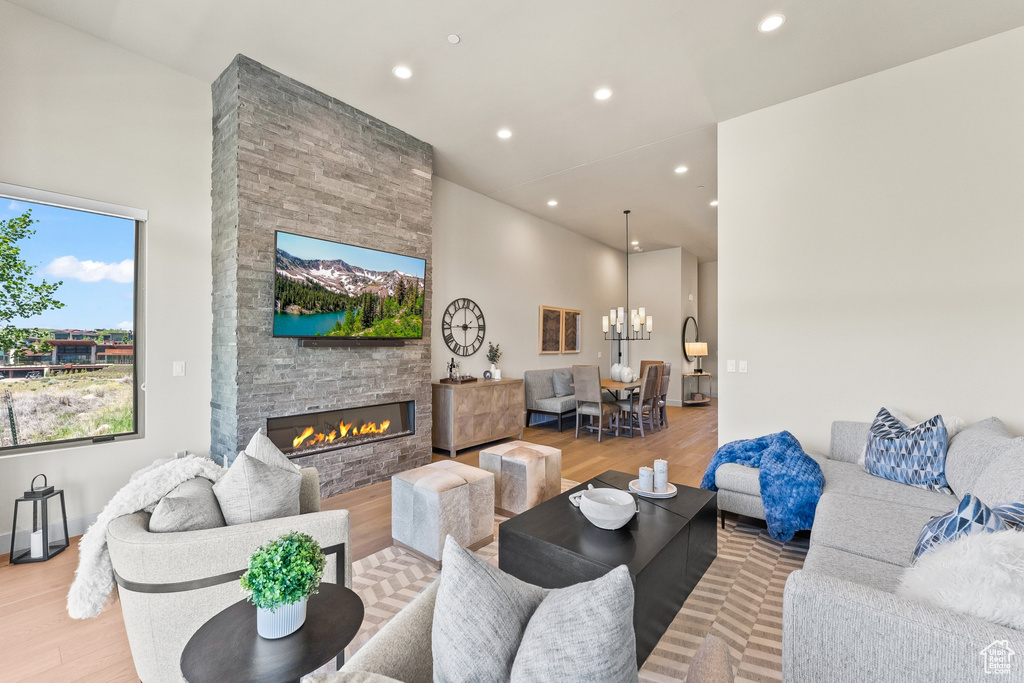 Living room featuring wood finished floors, a stone fireplace, recessed lighting, a chandelier, and a high ceiling