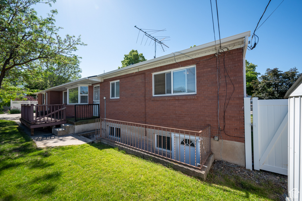 Rear view of house with a yard, a wooden deck, and brick siding