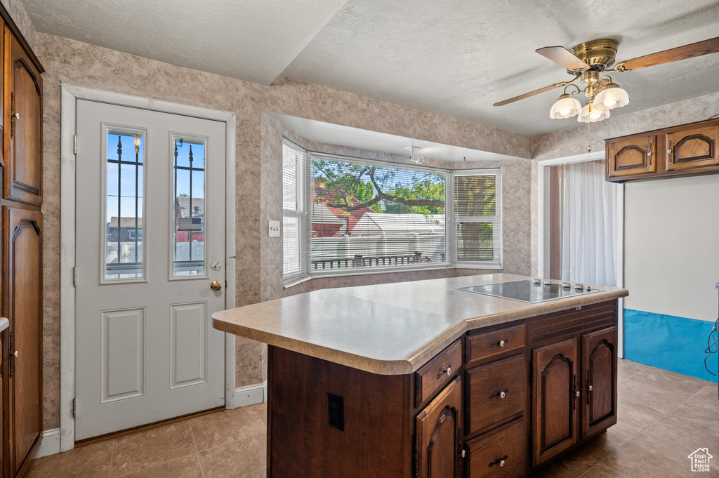 Kitchen featuring black electric stovetop, ceiling fan, light countertops, a kitchen island, and light tile patterned floors