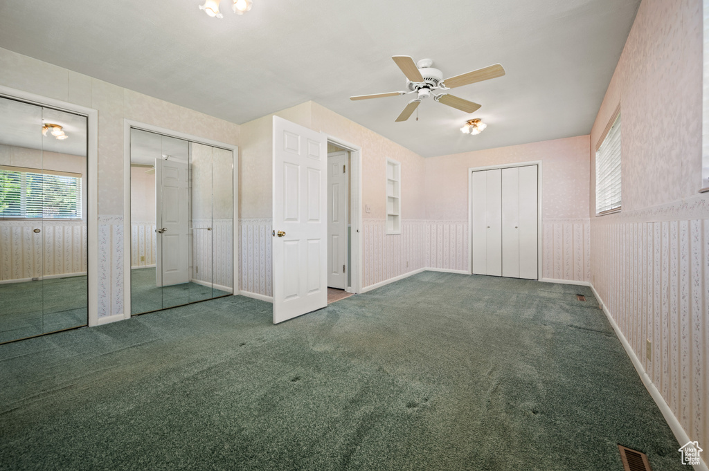 Unfurnished bedroom with multiple closets, carpet floors, a wainscoted wall, and ceiling fan