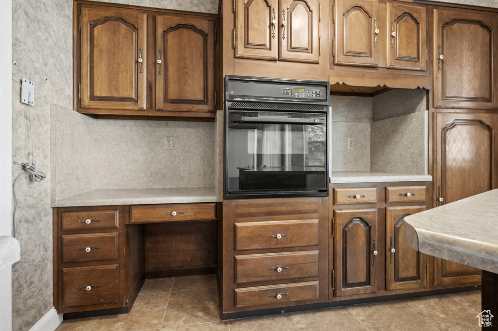 Kitchen with oven, light countertops, light tile patterned floors, and brown cabinetry