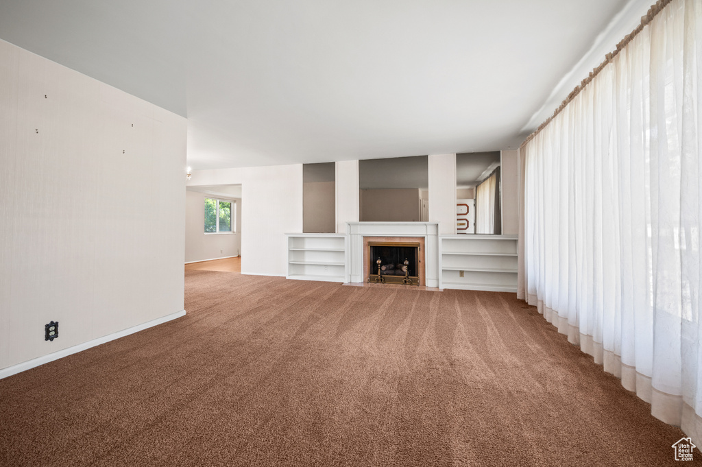 Unfurnished living room featuring light colored carpet, a fireplace with flush hearth, and baseboards