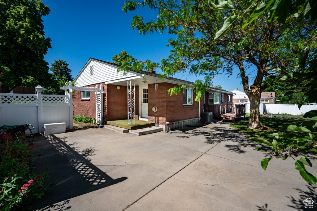 View of front of home with brick siding, a patio, and cooling unit