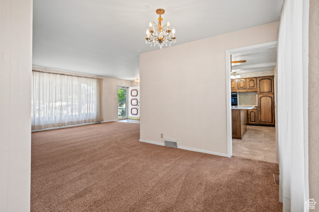 Unfurnished room with light colored carpet, a chandelier, and baseboards