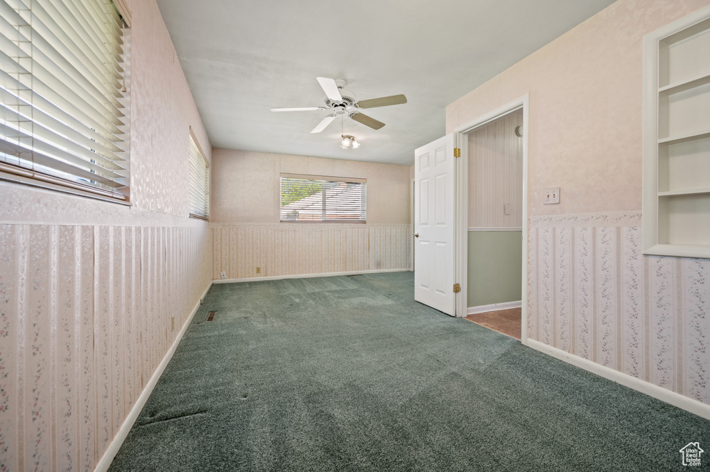Carpeted spare room with a wainscoted wall, ceiling fan, and wallpapered walls