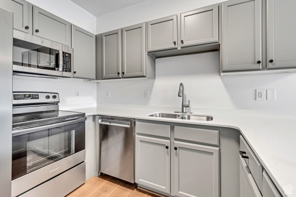 Kitchen with appliances with stainless steel finishes, gray cabinets, a sink, and light countertops
