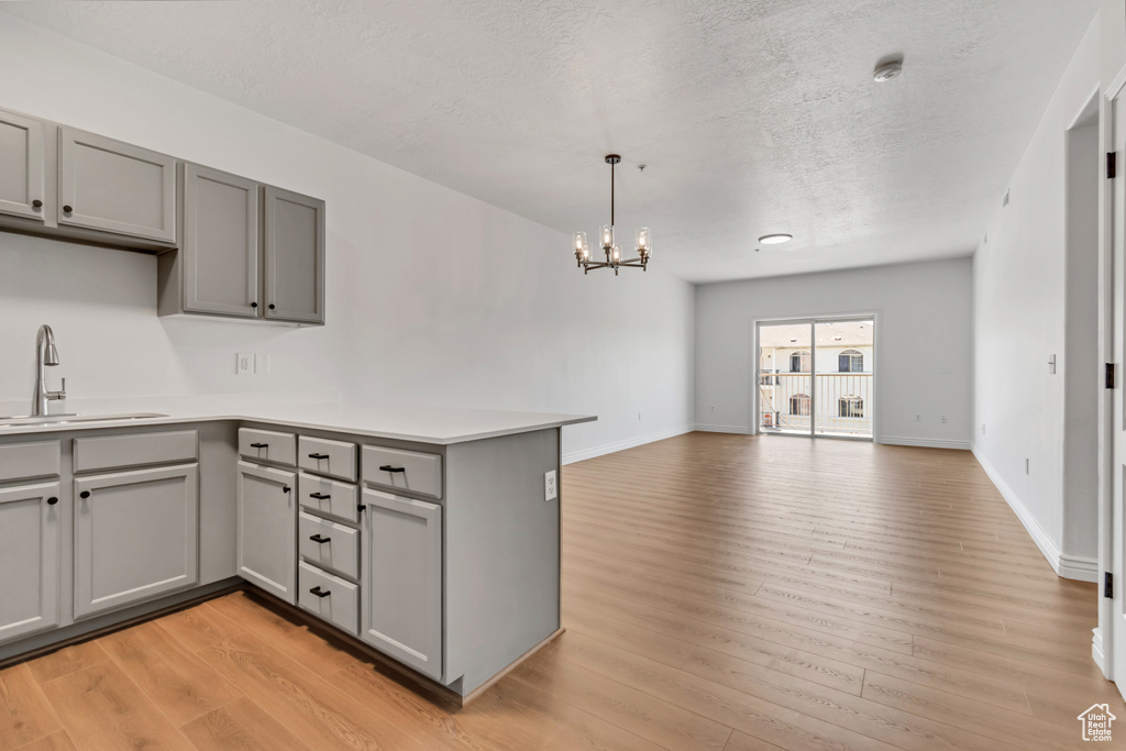 Kitchen featuring gray cabinetry, a sink, a peninsula, a chandelier, and light wood-style flooring