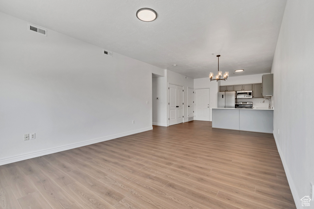 Unfurnished living room with a chandelier, baseboards, and light wood-type flooring