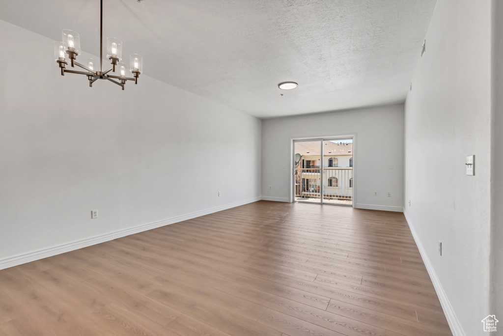 Unfurnished room with wood finished floors, a chandelier, baseboards, and a textured ceiling