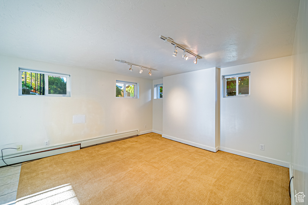 Spare room with rail lighting, light carpet, a baseboard heating unit, and baseboards