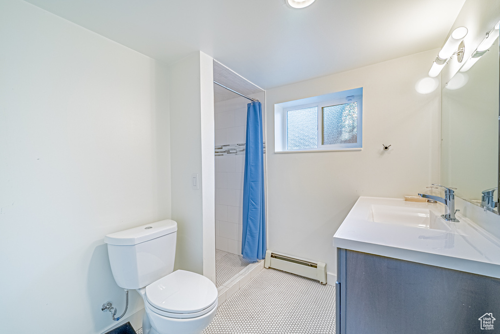 Bathroom featuring a baseboard radiator, toilet, vanity, tiled shower, and tile patterned floors