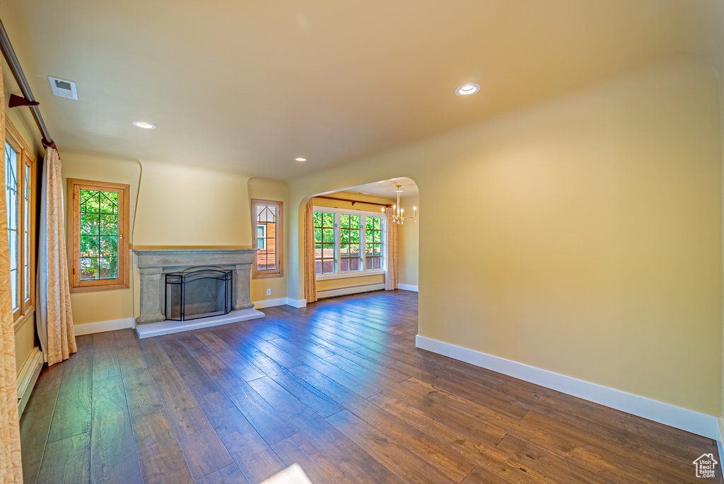 Unfurnished living room featuring a baseboard radiator, healthy amount of natural light, dark wood finished floors, recessed lighting, and a fireplace with raised hearth