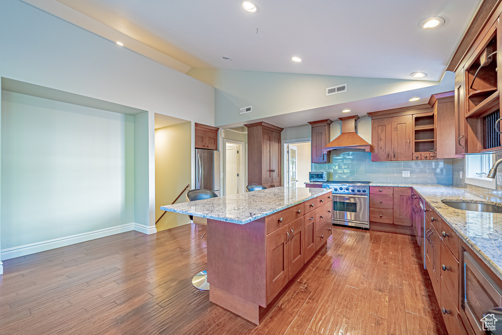 Kitchen featuring custom range hood, appliances with stainless steel finishes, a sink, lofted ceiling, and open shelves