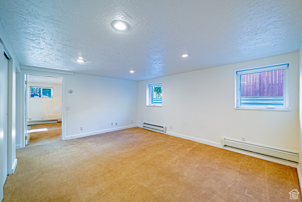 Spare room featuring a baseboard heating unit, baseboard heating, a textured ceiling, baseboards, and carpet floors