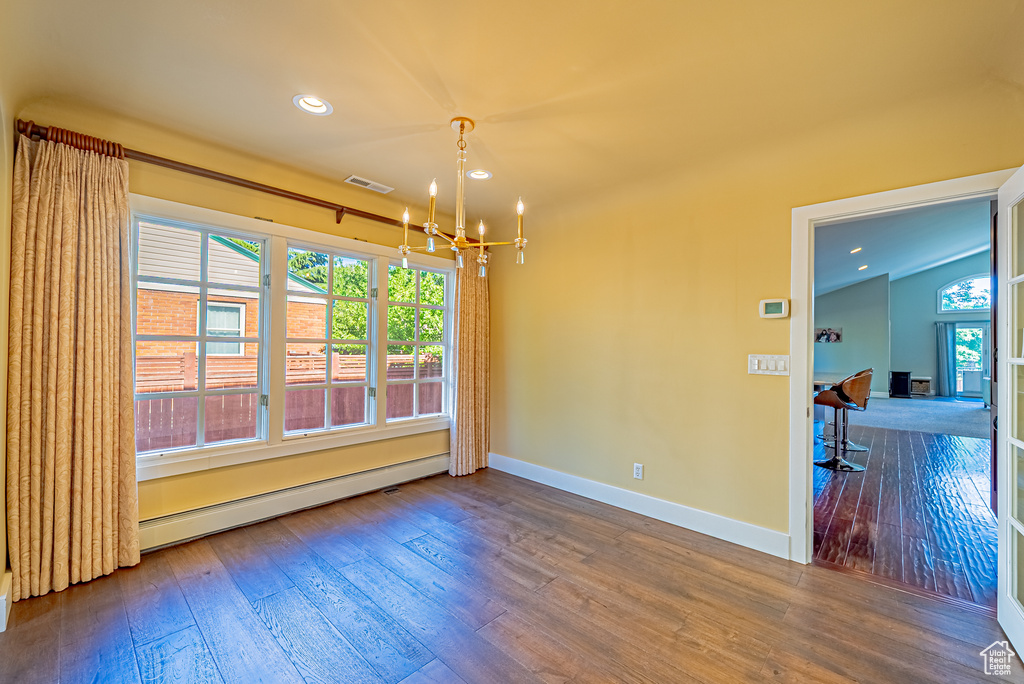 Empty room with a chandelier, hardwood / wood-style floors, baseboards, a baseboard radiator, and recessed lighting