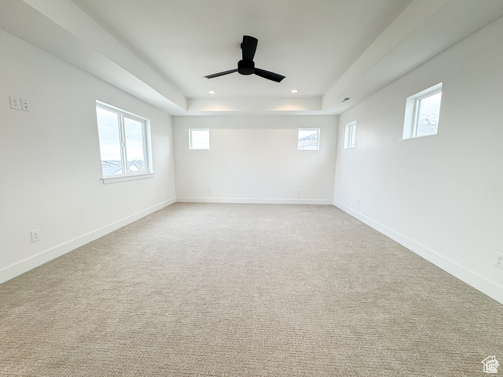 Carpeted empty room with healthy amount of natural light, recessed lighting, ceiling fan, a tray ceiling, and baseboards