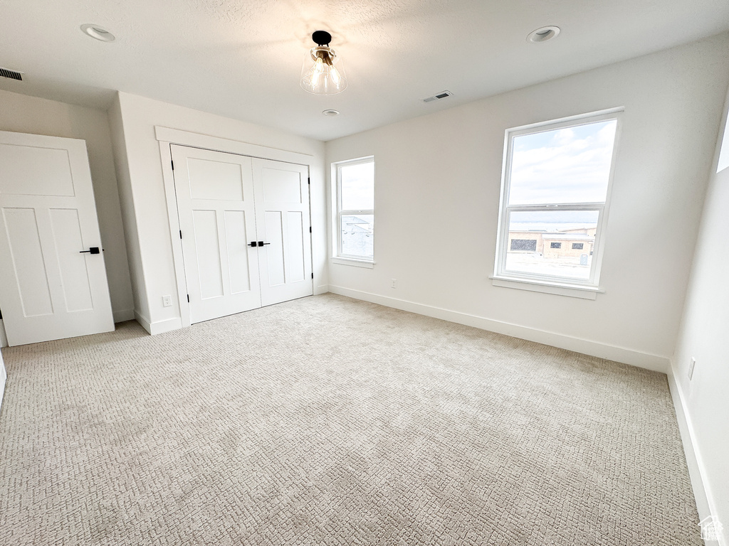Unfurnished bedroom with baseboards, light carpet, and a closet