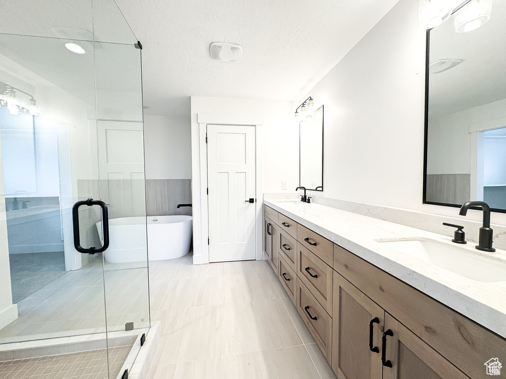 Full bath with double vanity, a freestanding bath, a stall shower, and a textured ceiling