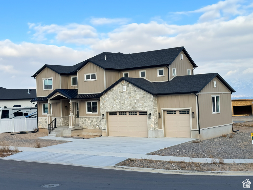 View of front facade featuring a standing seam roof, driveway, an attached garage, metal roof, and stone siding