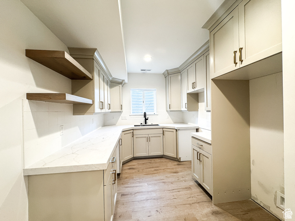 Kitchen with a sink, open shelves, light wood-type flooring, gray cabinetry, and backsplash