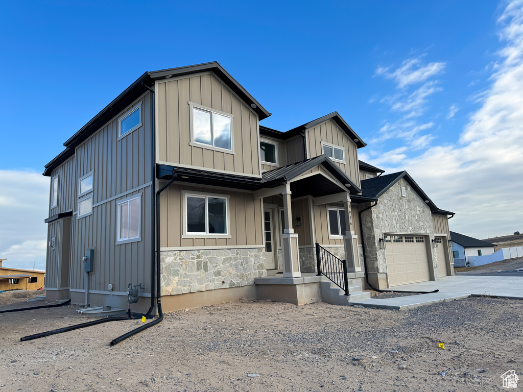 View of front facade featuring board and batten siding, stone siding, driveway, and an attached garage