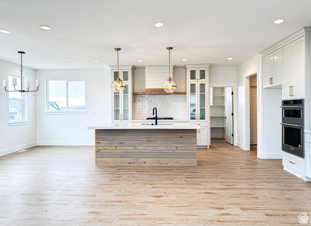 Kitchen with double wall oven, baseboards, light wood finished floors, decorative backsplash, and recessed lighting