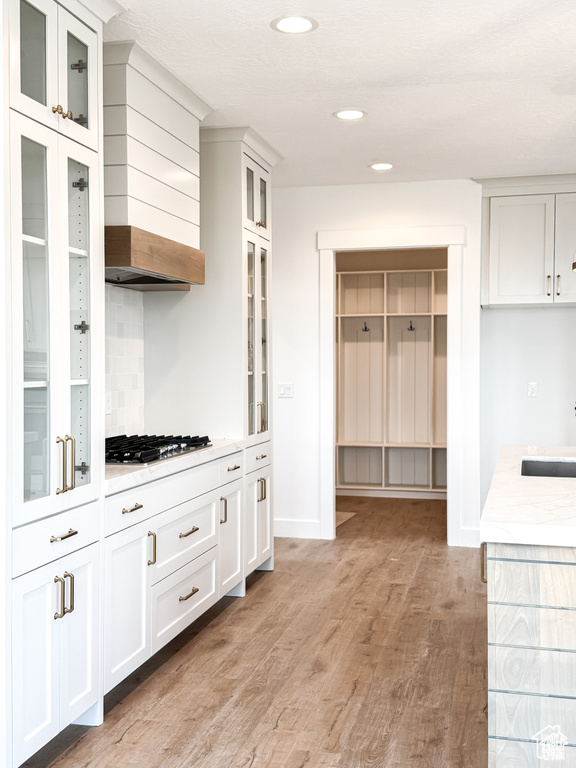 Kitchen with light countertops, light wood-style floors, white cabinetry, recessed lighting, and wall chimney exhaust hood