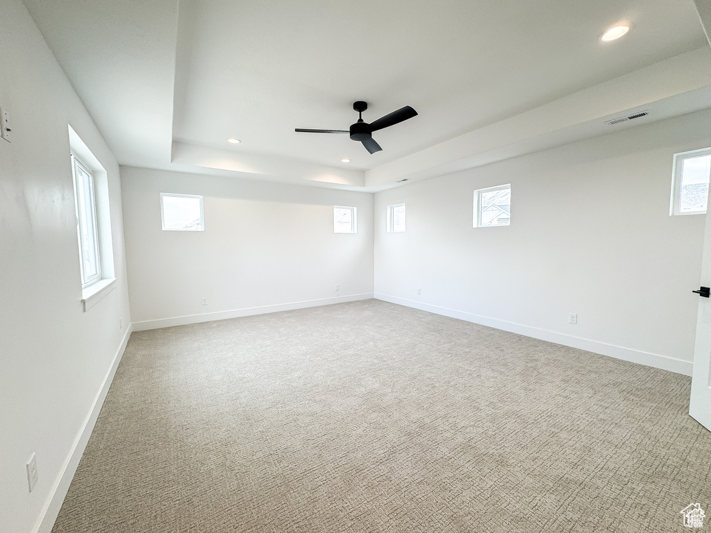 Carpeted spare room featuring a tray ceiling, recessed lighting, ceiling fan, baseboards, and healthy amount of natural light