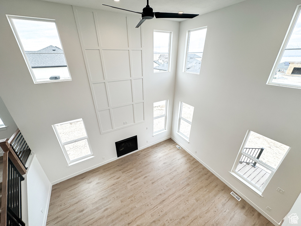Unfurnished living room featuring a fireplace, wood finished floors, a ceiling fan, baseboards, and a towering ceiling