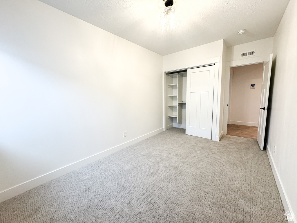 Unfurnished bedroom with light carpet, a closet, and baseboards