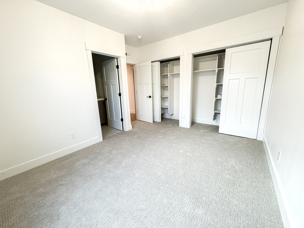 Unfurnished bedroom featuring two closets, light colored carpet, and baseboards
