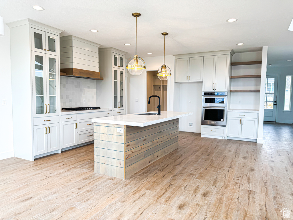 Kitchen featuring a sink, stainless steel appliances, backsplash, light wood-type flooring, and wall chimney exhaust hood
