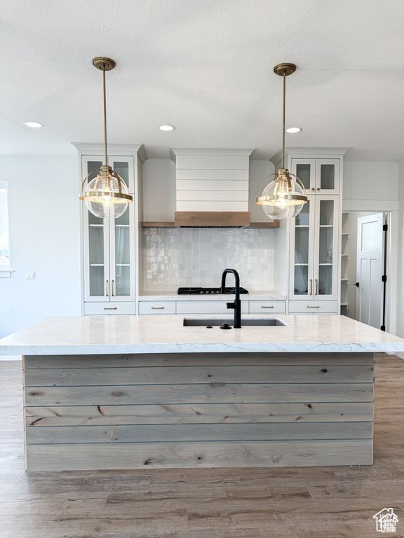 Kitchen featuring wood finished floors, a sink, backsplash, an island with sink, and recessed lighting