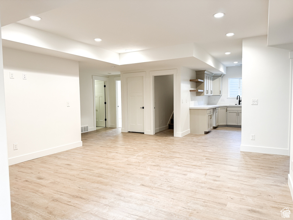 Unfurnished living room featuring a sink, light wood finished floors, recessed lighting, and baseboards